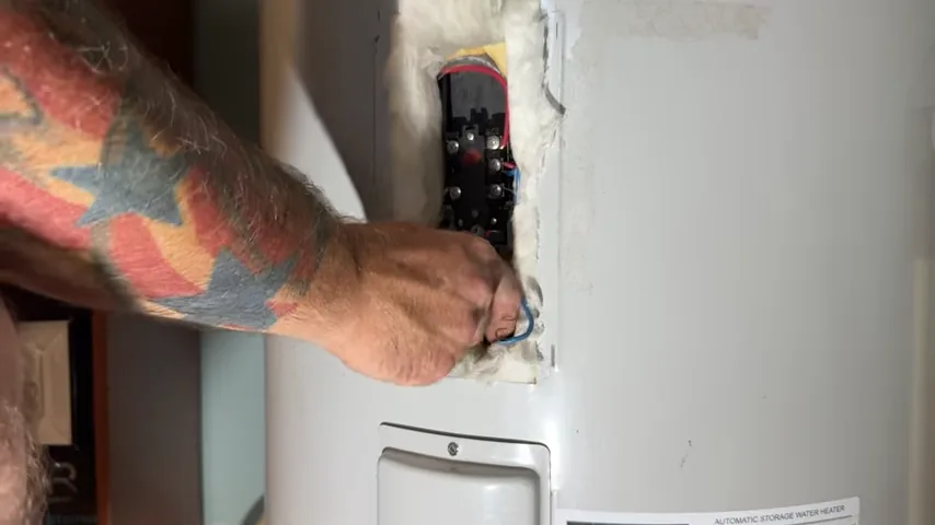 Hand working at an open electric water heater heating-element access panel