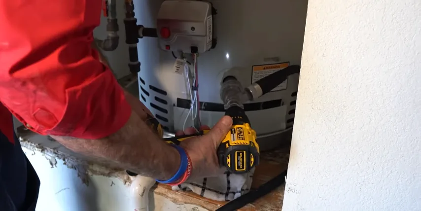 Person using a power drill near the lower service opening of a tank water heater